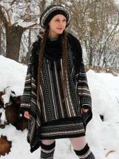 Frau mit Zöpfen im Schnee, trägt Alpaka-Poncho mit Jacquardmuster, schwarzer Basis, dazu Baskenmütze, Rock und passende Beinstulpen.